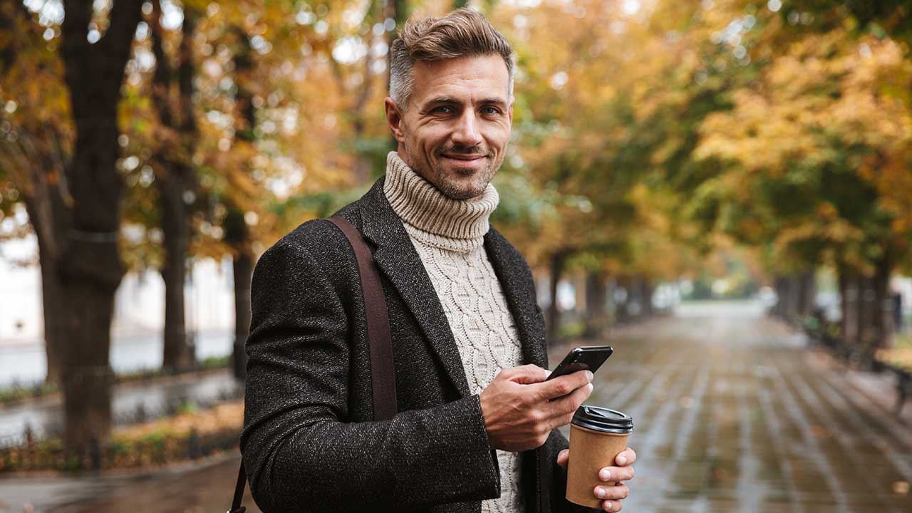 Mann mit Smartphone und Coffee-to-Go läuft Straße entlang