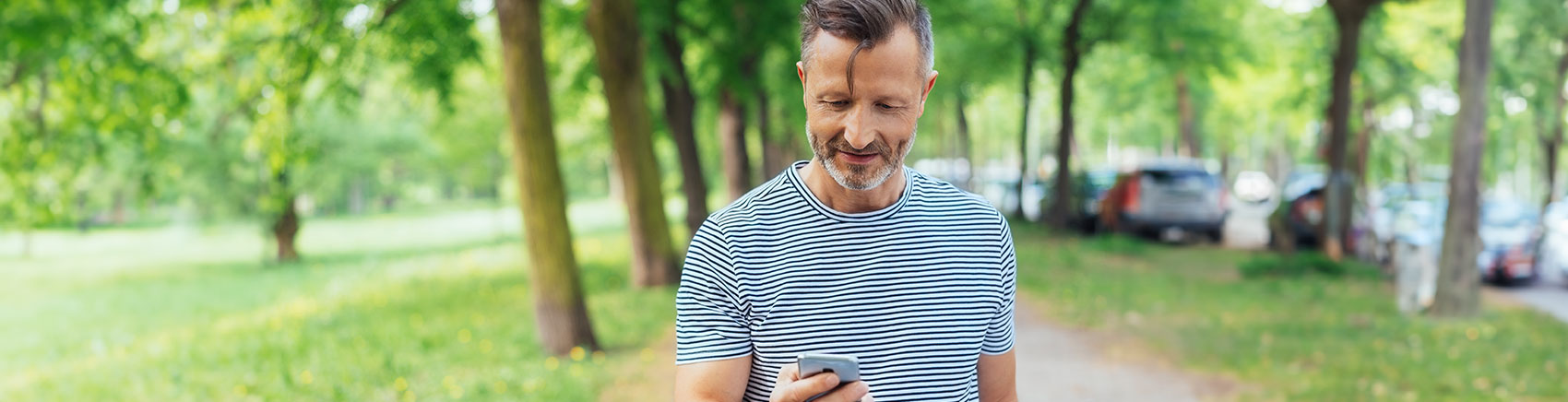 Mann steht interessiert vor einem Park und blickt auf sein Handy