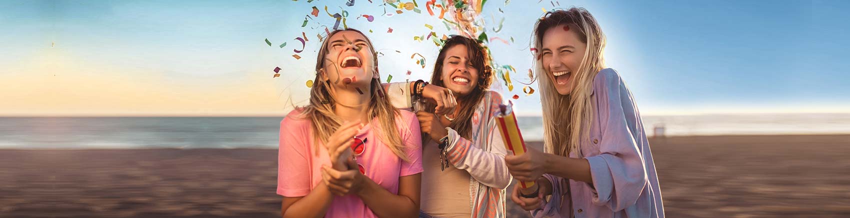 Drei Frauen, die sich am Strand über eine Konfettikanone freuen